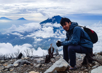 Side view of young man on rock against sky