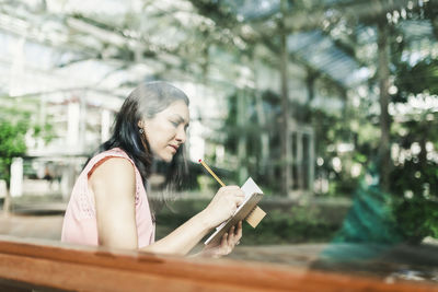 Beautiful agronomical engineer taking notes sitting in the greenhouse