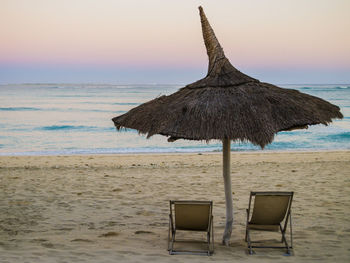 Chair on beach against sky during sunset