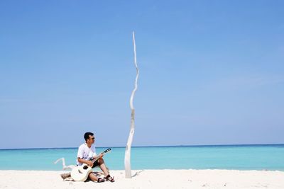 Man sitting at beach against sky