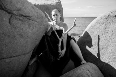 Woman sitting on rock with branch against sea