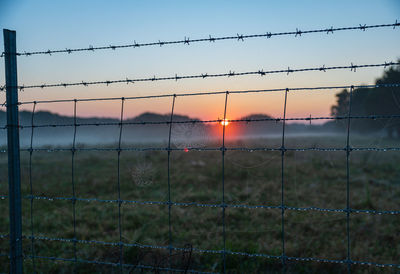 Close-up of barbed wire fence on field against sky during sunset