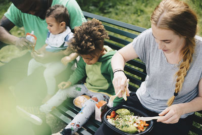 High angle view of family having food while sitting on bench at park