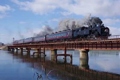 Train on bridge over river against sky