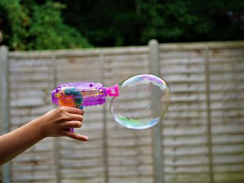 Cropped image of hand holding bubbles against blurred background