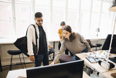 Female programmer showing computer to coworkers against window in office