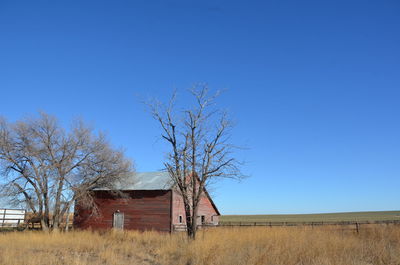 Abandoned barn on field against clear blue sky