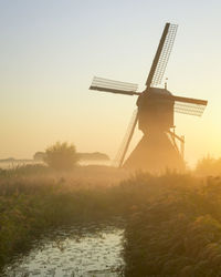 Traditional windmill on landscape against sky during sunset