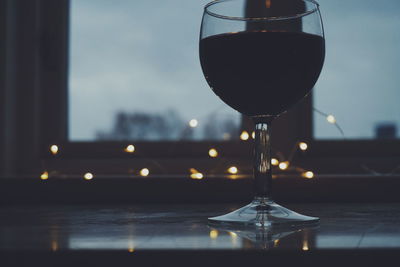Close-up of red wine in glass by illuminated string lights on window sill