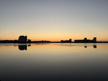 Scenic view of lake by buildings against sky during sunset