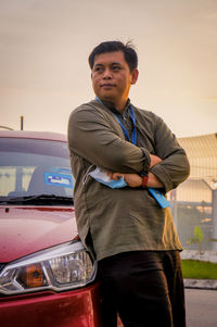 Portrait of young man standing on car against sky