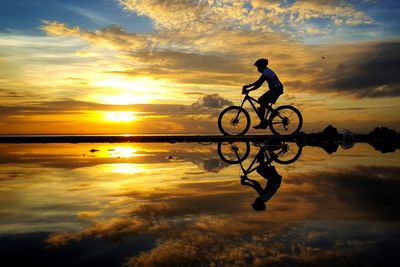 Silhouette man with bicycle against sky during sunset