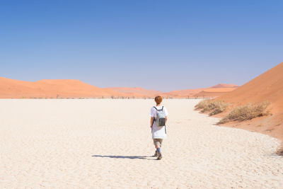 Rear view of mature woman walking at desert against sky