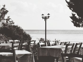 Empty chairs and tables at restaurant by sea against sky