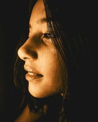 Side view of beautiful young woman against black background