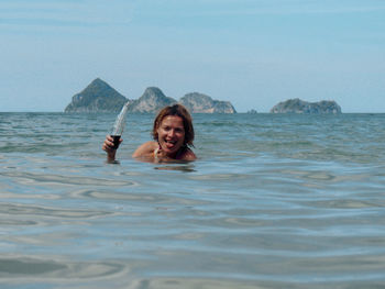 Portrait of smiling woman swimming in sea against sky