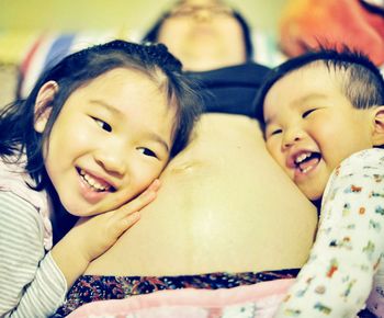 Smiling siblings listening to abdomen of mother