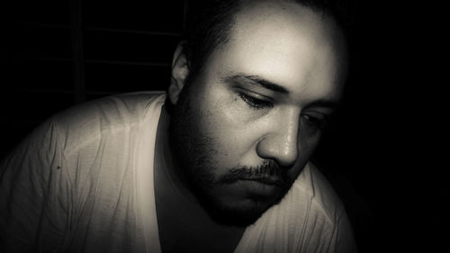 Close-up of thoughtful man looking down against black background