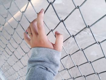 Cropped hand of woman holding chainlink fence