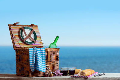 Food and drink with picnic basket on table by sea against clear sky