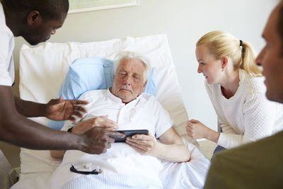 Male nurse showing digital tablet to senior man and couple at hospital ward