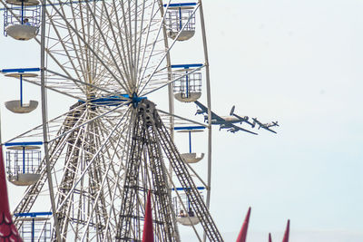 Low angle view of airplanes flying by ferris wheel against clear sky