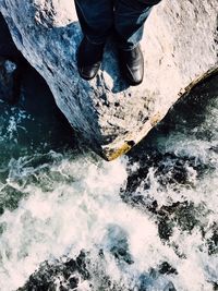 Low section of man standing on rock over river during sunny day