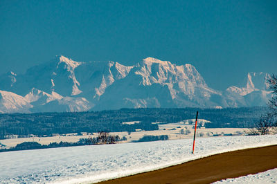 Scenic view of snowcapped mountains by sea against clear blue sky