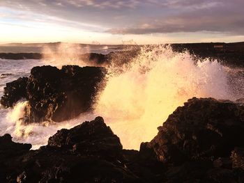 Waves splashing on rocks at shore against sky