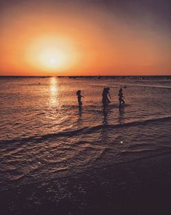 Silhouette people on beach against sky during sunset