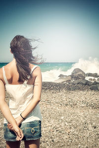 Rear view of woman sitting on beach against sky