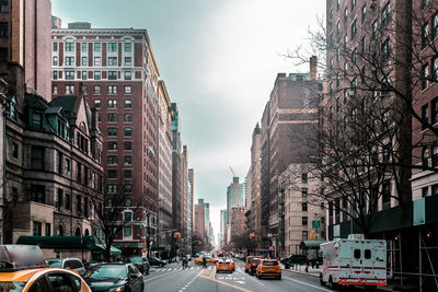 Vehicles on road by buildings against sky