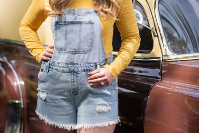 Woman standing by classic car with hand on hip