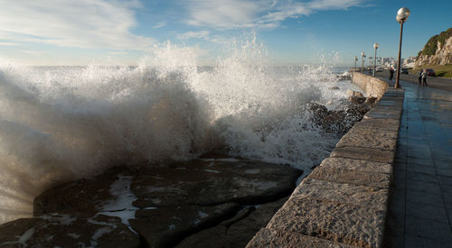 Waves splashing on shore against sky