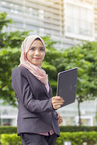 Thoughtful businesswoman holding digital tablet while standing against office building