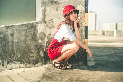 Full length portrait of woman crouching against wall