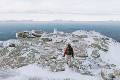 Rear view of backpacker with camera walking on snow covered rocks