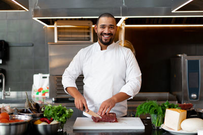 Portrait of smiling young man preparing food in commercial kitchen