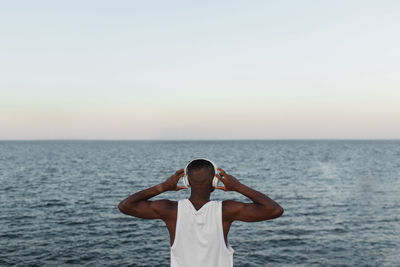 Full body back view of african american runner warming up before running while listening to music in wireless headphones