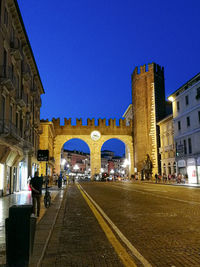 People walking in illuminated building against clear blue sky