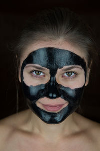 Close-up portrait of young woman with facial mask against black background
