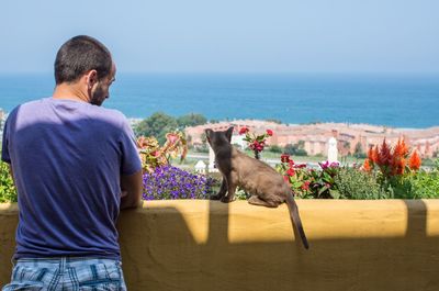 Rear view of man with cat looking at seascape