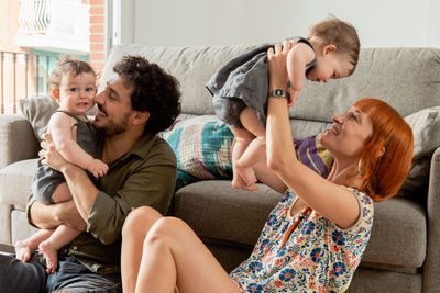 Happy multiethnic young mother and father hugging cute smiling twin babies while sitting on floor during weekend at home