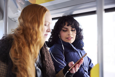 Female friends sitting in bus together and looking at cell phone