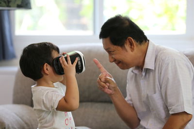 Boy with grandfather wearing virtual reality simulator in living room at home
