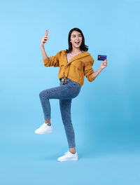 Portrait of smiling young woman using smart phone against blue background