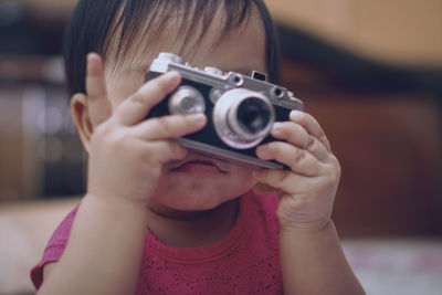 Close-up of cute baby girl photographing with camera at home