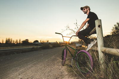 Side view of man sitting with bicycle on road during sunset