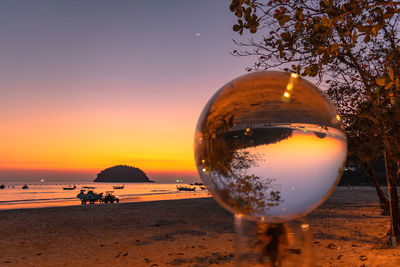 Close-up of beer glass on beach against sky during sunset