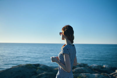 Side view of young woman standing by sea against clear sky